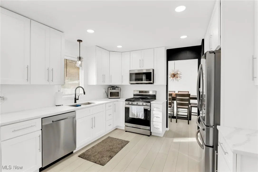 Kitchen with stainless steel appliances, decorative light fixtures, white cabinets, light wood-type flooring, and recessed lighting
