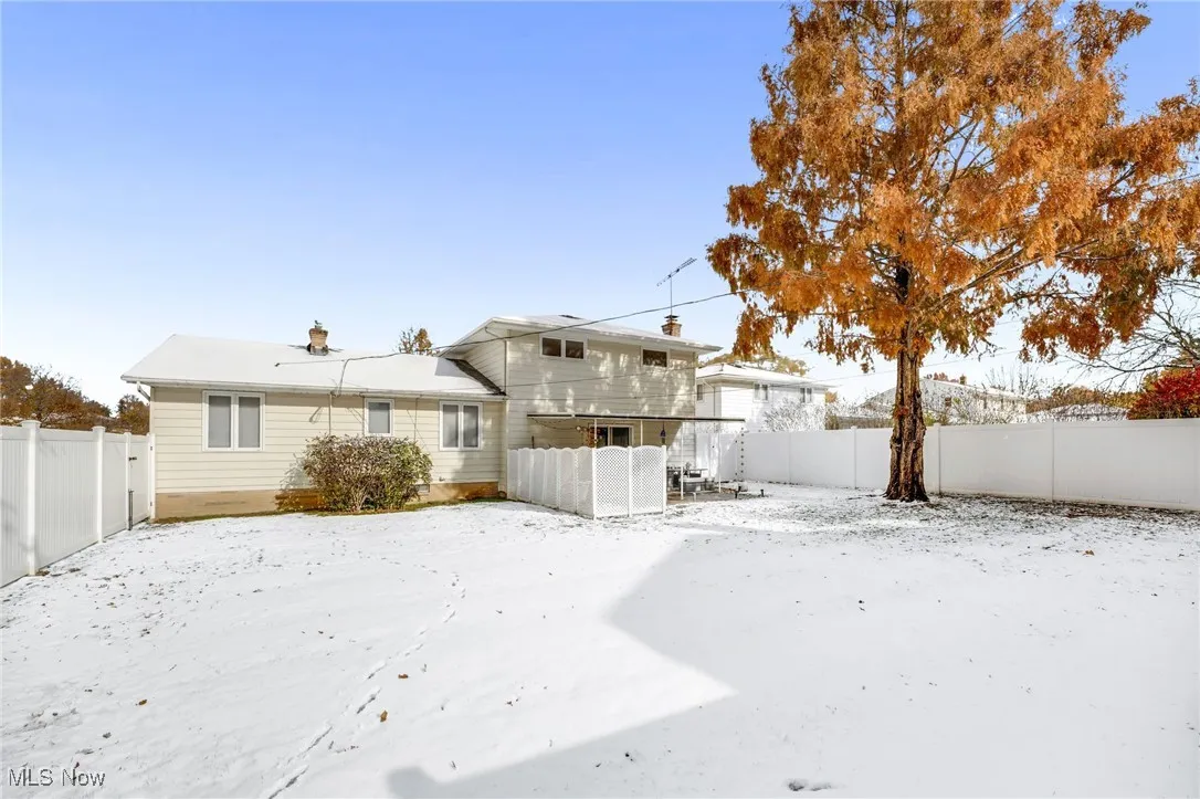 Snow covered back of property with a fenced backyard and a chimney
