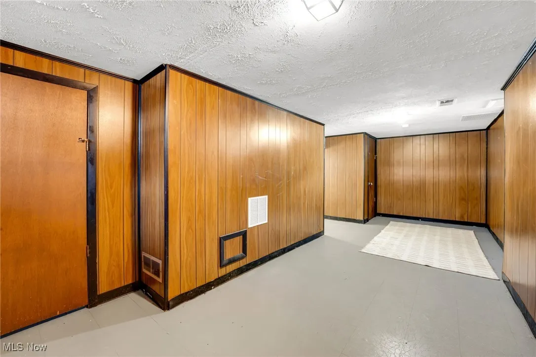 Rec room with wood walls, a textured ceiling, and light floors