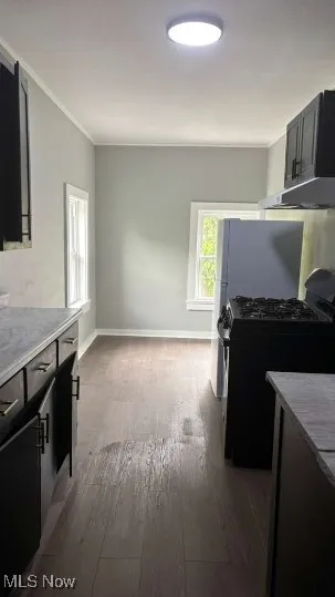 Kitchen with black gas stove, light countertops, ornamental molding, dark wood finished floors, and dark cabinets