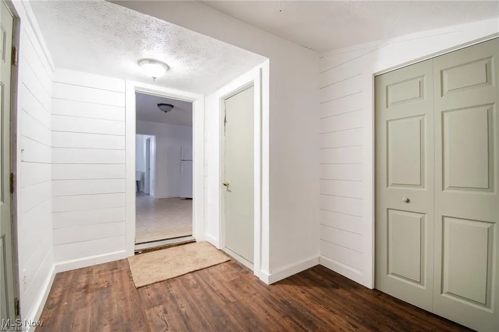 Hallway featuring a textured ceiling, dark wood finished floors, and wood walls