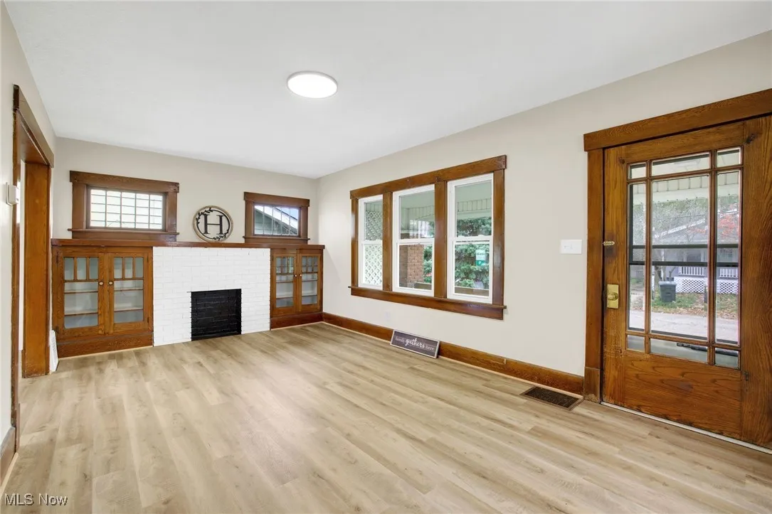 Unfurnished living room with healthy amount of natural light, light wood finished floors, and a brick fireplace