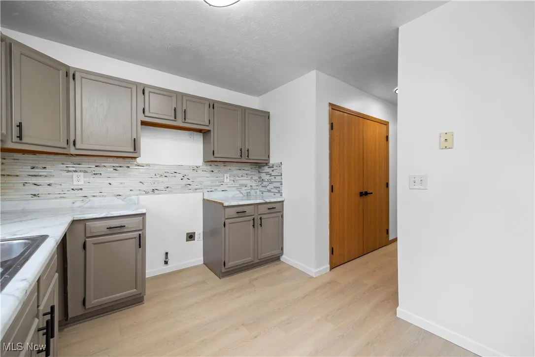 Kitchen featuring gray cabinets, light wood-style flooring, decorative backsplash, light countertops, and a textured ceiling