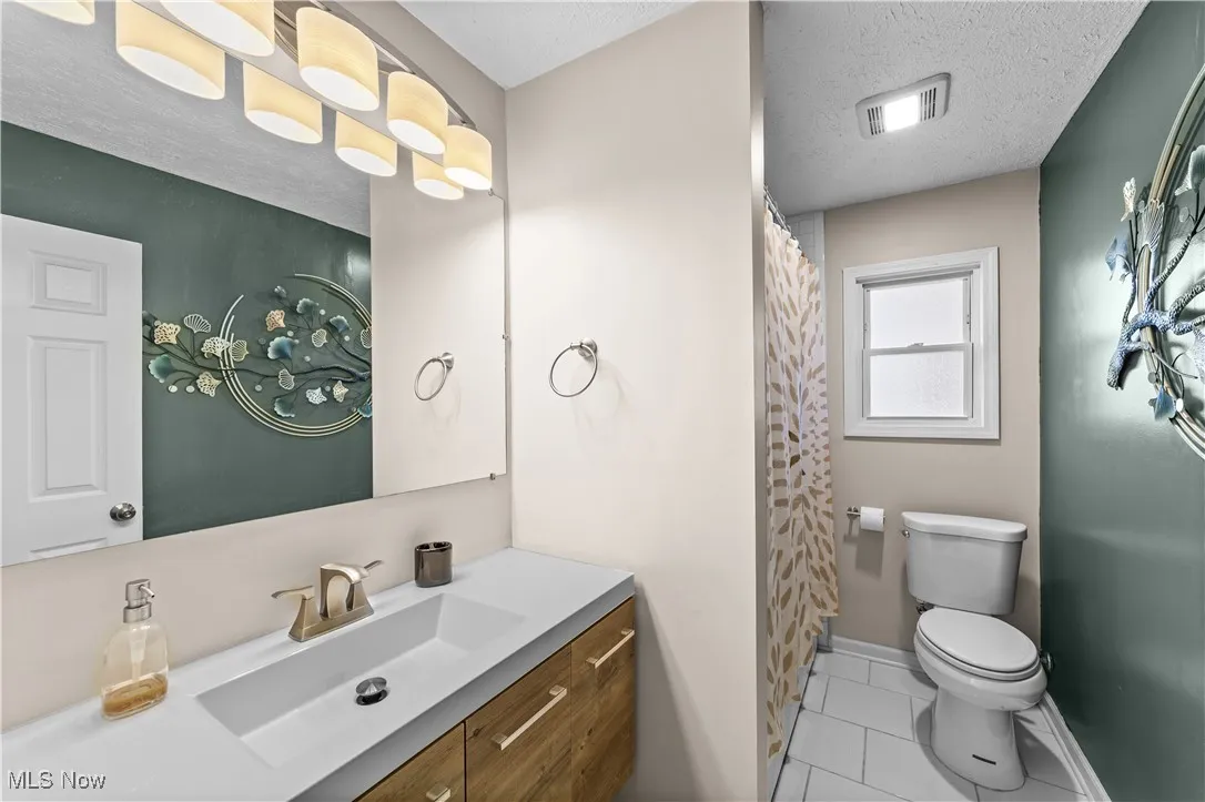 Full bathroom with a textured ceiling, curtained shower, light tile patterned floors, and vanity