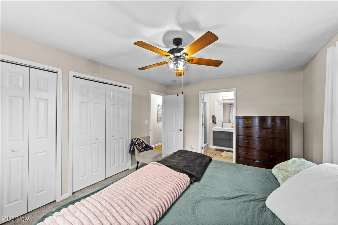 Carpeted bedroom featuring multiple closets, ceiling fan, and connected bathroom