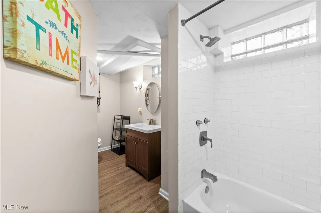 Bathroom featuring washtub / shower combination, dark wood-style floors, and vanity
