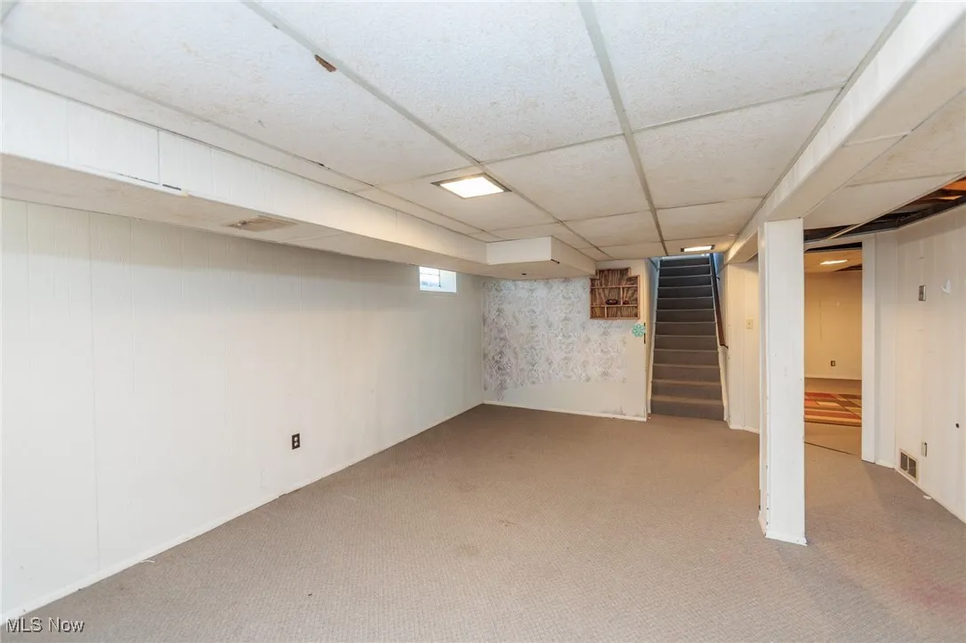 Below grade area with carpet floors, a drop ceiling, and stairway