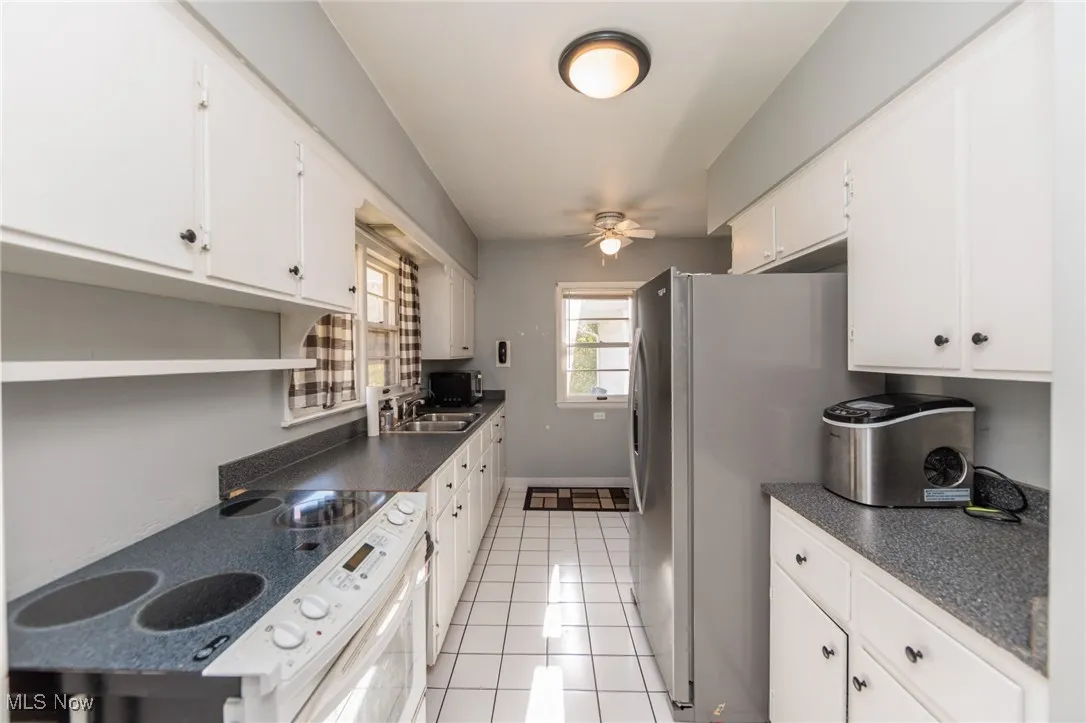 Kitchen with dark countertops, white electric range, light tile patterned floors, and white cabinetry