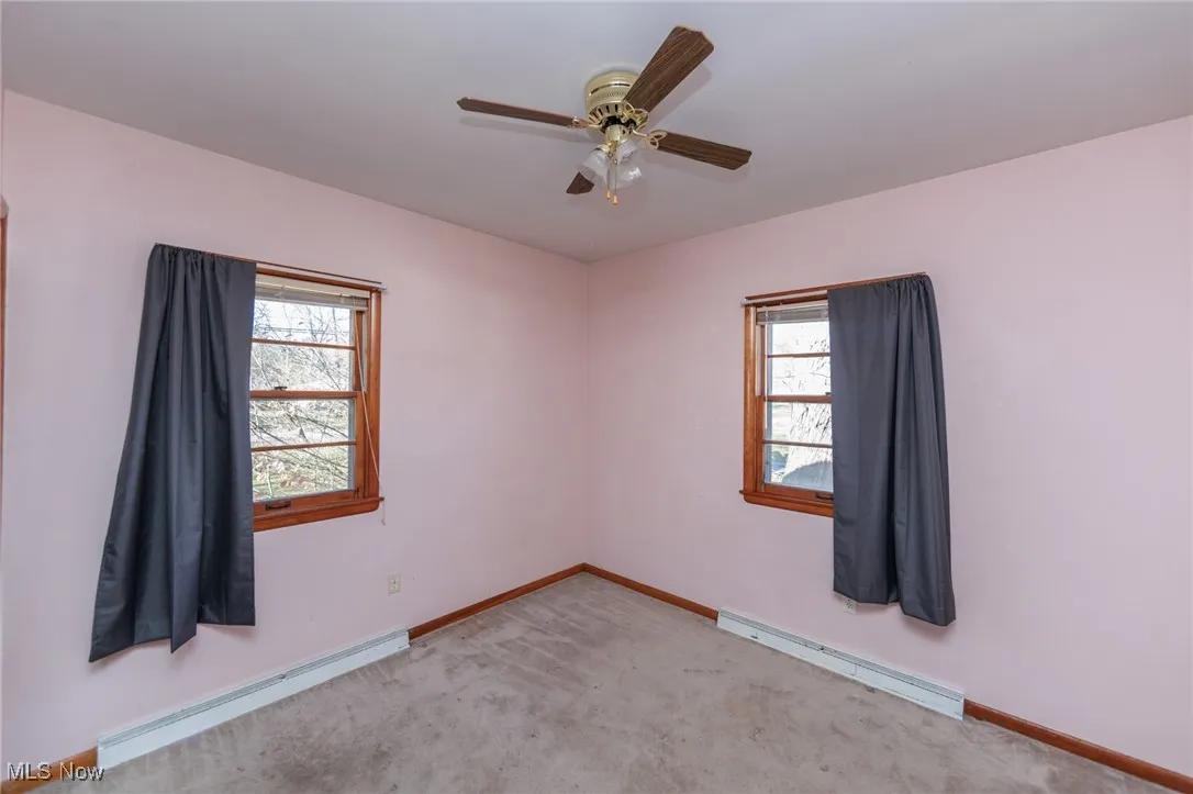 Empty room featuring baseboard heating, carpet, and ceiling fan