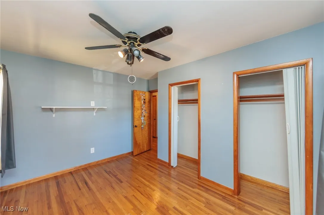 Unfurnished bedroom with multiple closets, wood finished floors, and ceiling fan