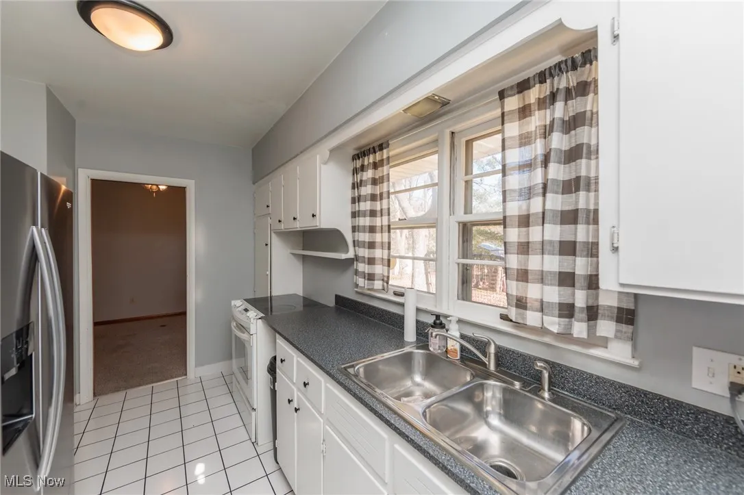 Kitchen featuring stainless steel refrigerator with ice dispenser, white cabinets, electric range, dark countertops, and light tile patterned floors