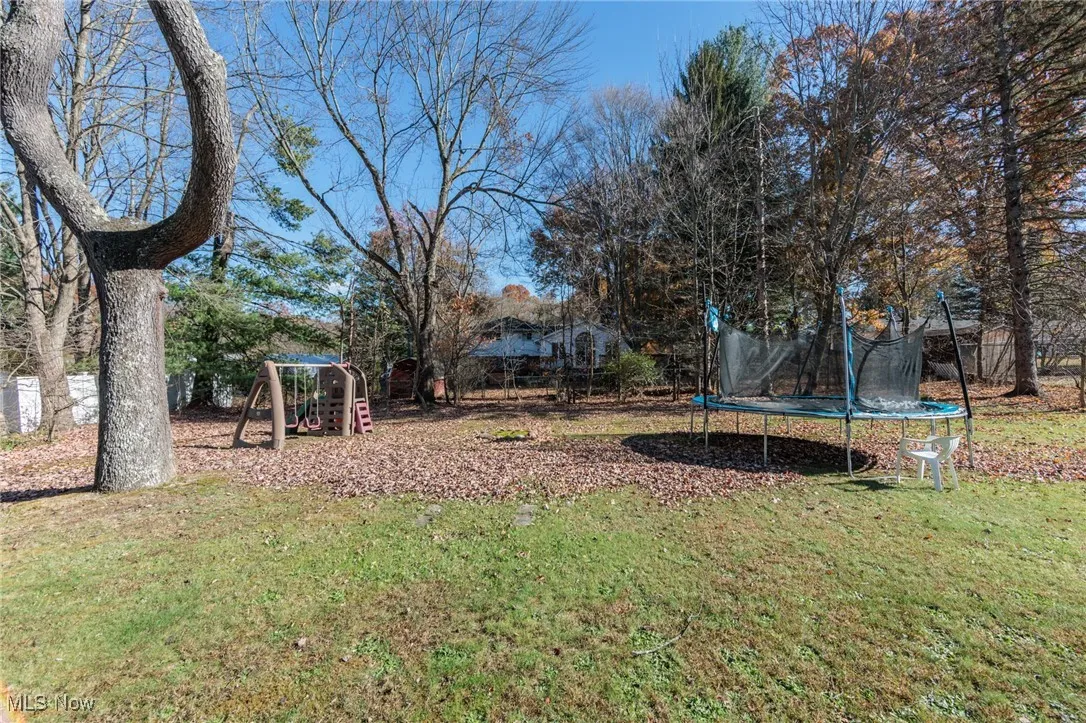 View of green lawn featuring a trampoline, a playground, and view of wooded area