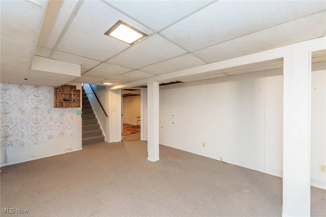 Finished below grade area with carpet flooring, a paneled ceiling, and stairway