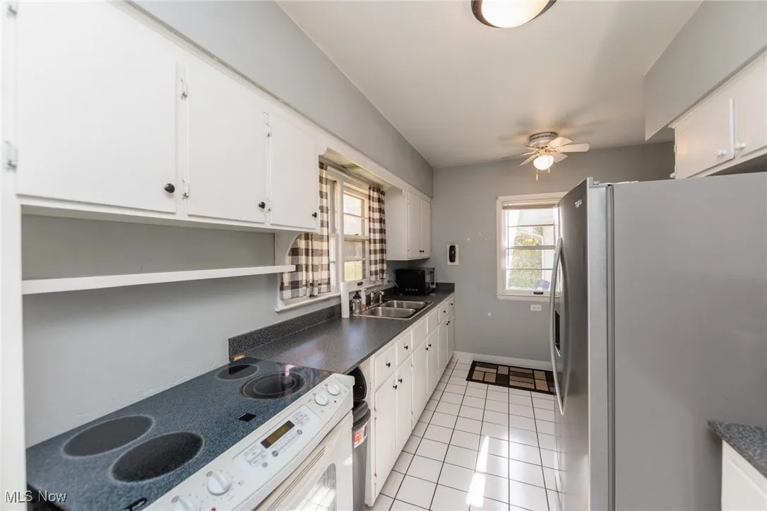 Kitchen with stainless steel fridge with ice dispenser, dark countertops, white electric stove, light tile patterned flooring, and white cabinets