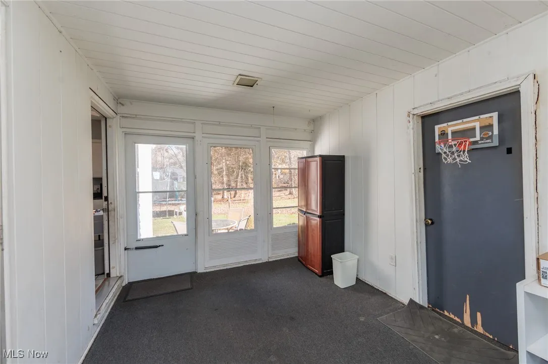 Doorway to outside featuring carpet flooring, wooden walls, and wooden ceiling