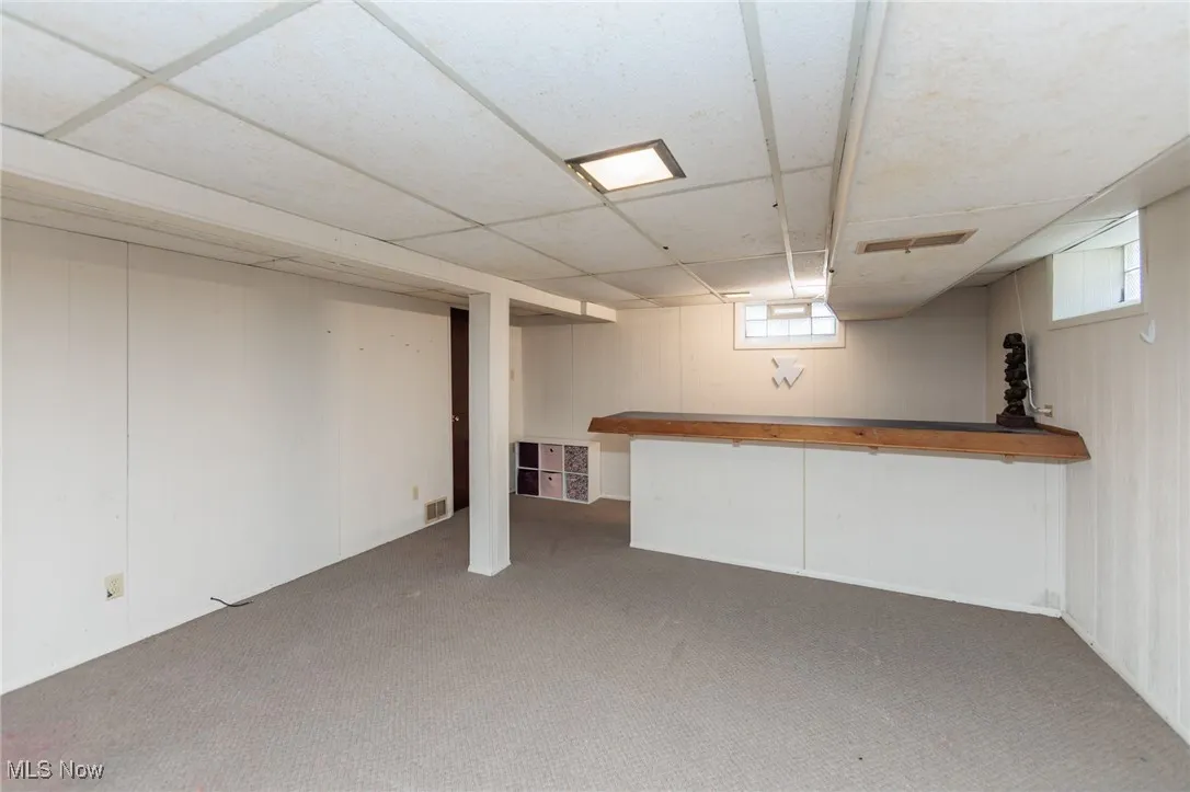 Basement featuring a bar, carpet floors, and a drop ceiling