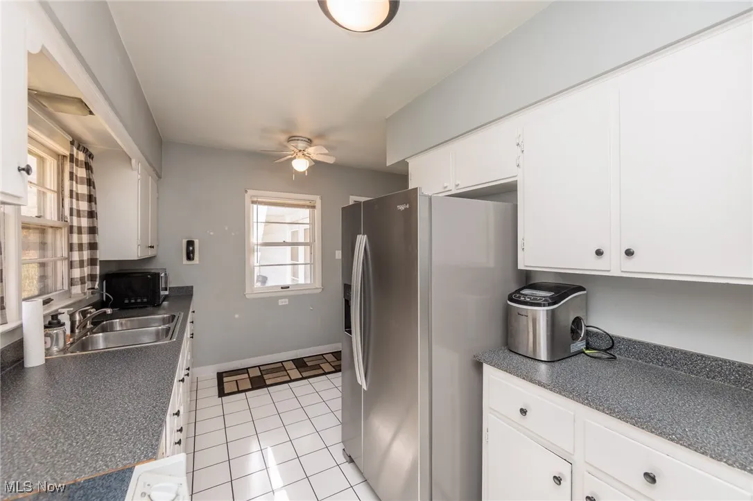 Kitchen with white cabinetry, dark countertops, stainless steel fridge, a ceiling fan, and light tile patterned flooring