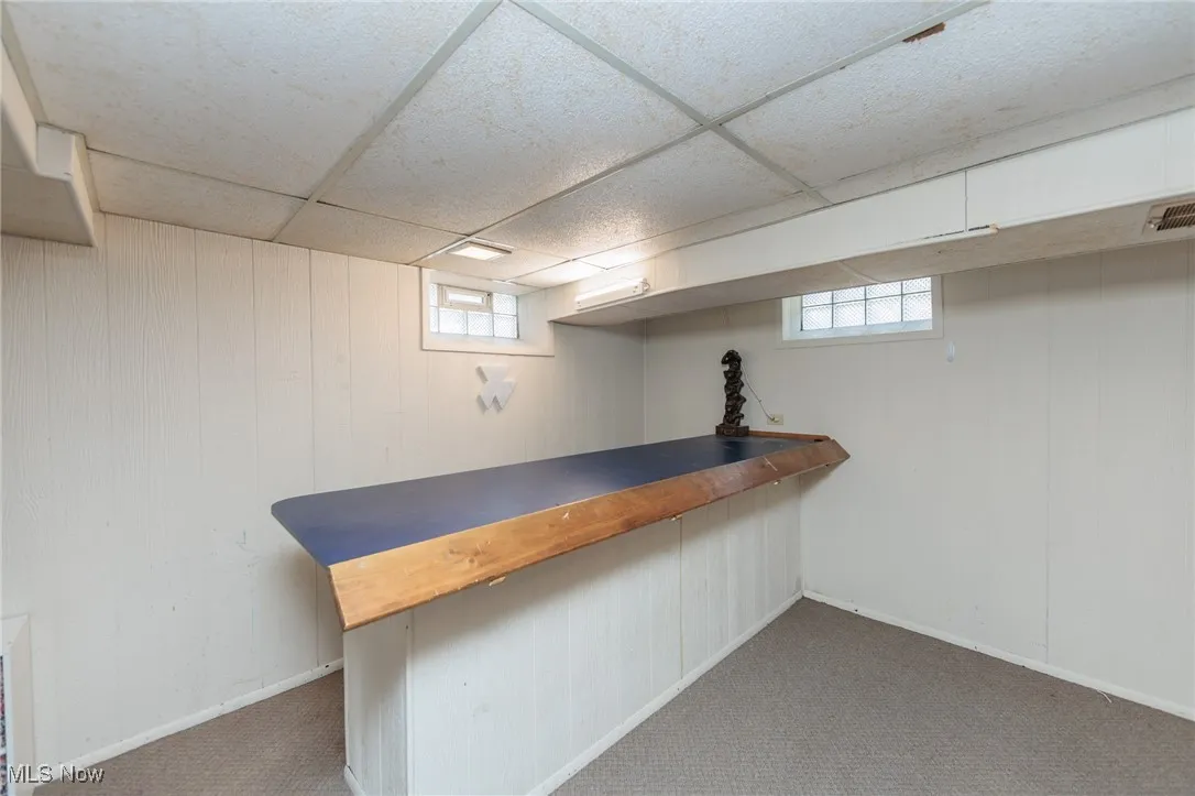 Bar featuring wooden counters, dark colored carpet, a drop ceiling, and wood walls