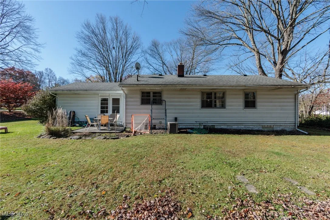 Rear view of house with a chimney, a lawn, and a patio