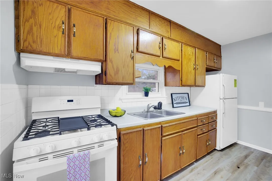Kitchen featuring white appliances, brown cabinets, light countertops, light wood-style flooring, and under cabinet range hood