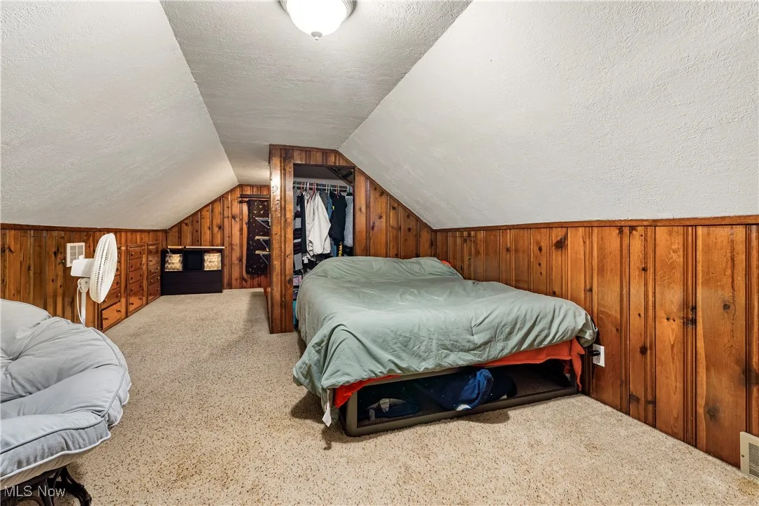 Carpeted bedroom featuring wooden walls, a textured ceiling, and lofted ceiling