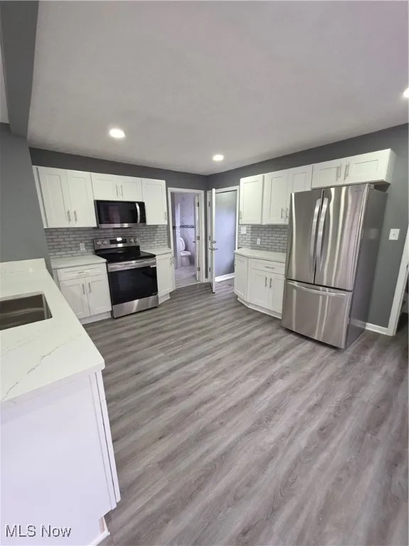 Kitchen with fridge, stove, white cabinets, light wood-style floors, and recessed lighting