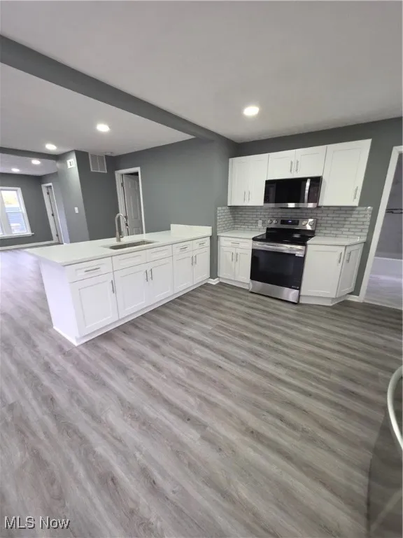 Kitchen with light wood-style floors, range, white cabinetry, backsplash, and open floor plan