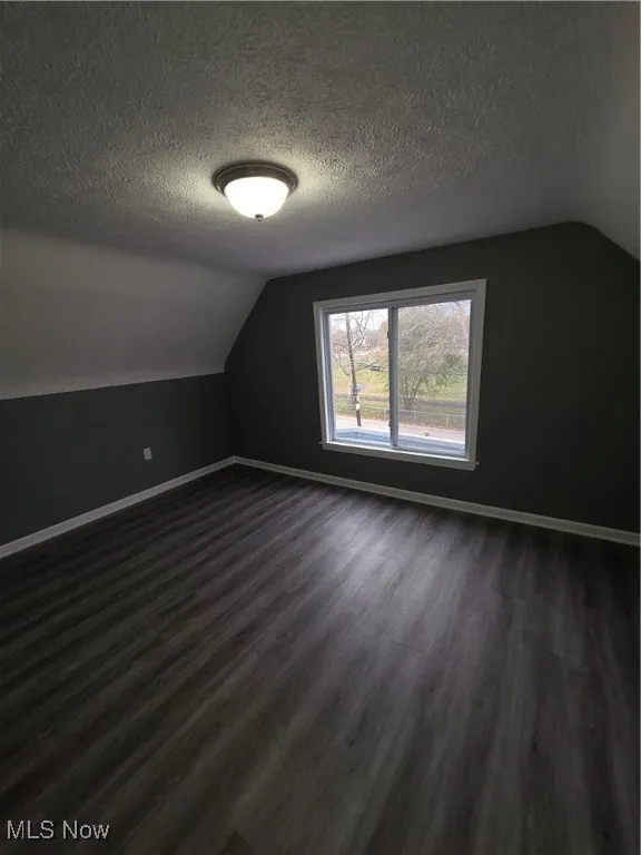 Bonus room featuring lofted ceiling, dark wood-style flooring, and a textured ceiling