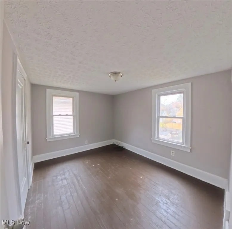 Unfurnished room featuring dark wood-style flooring and a textured ceiling