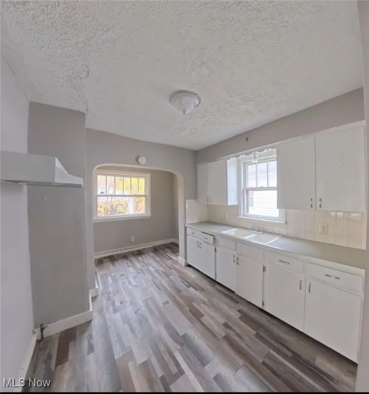 Kitchen with light countertops, white cabinets, healthy amount of natural light, light wood finished floors, and a textured ceiling