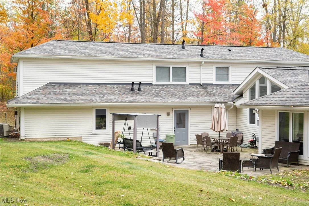 Back of house with a lawn, a patio, and roof with shingles