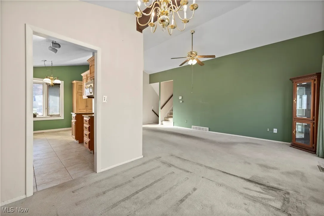 Unfurnished room with a chandelier, light colored carpet, light tile patterned flooring, ceiling fan, and stairway