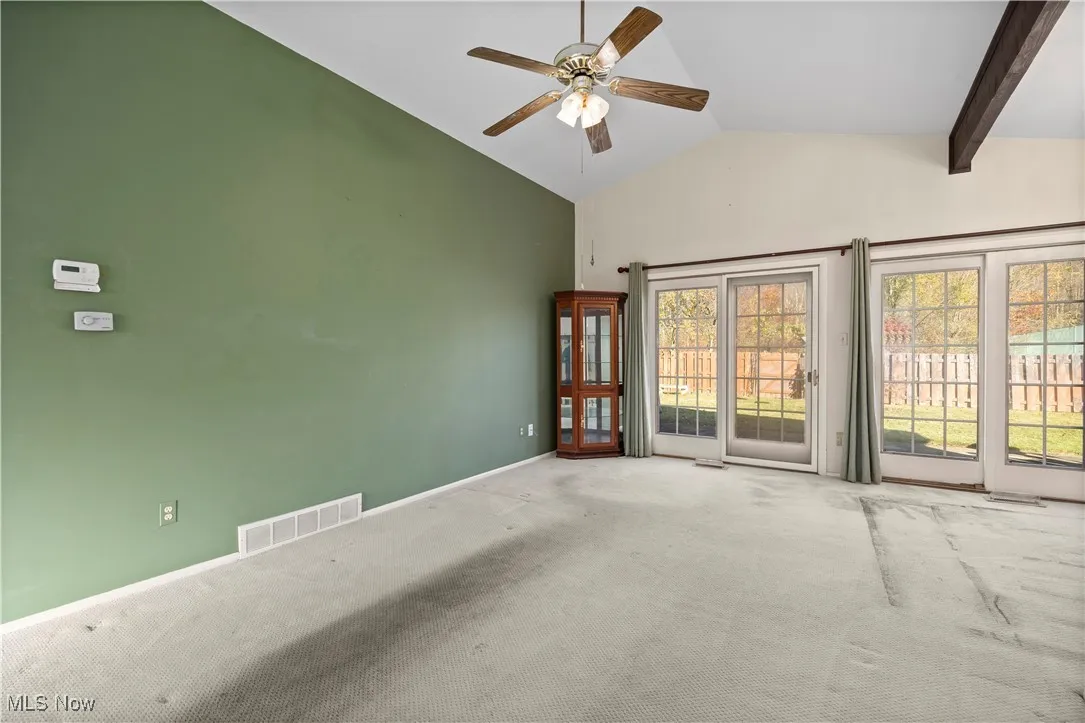 Carpeted spare room with ceiling fan and high vaulted ceiling