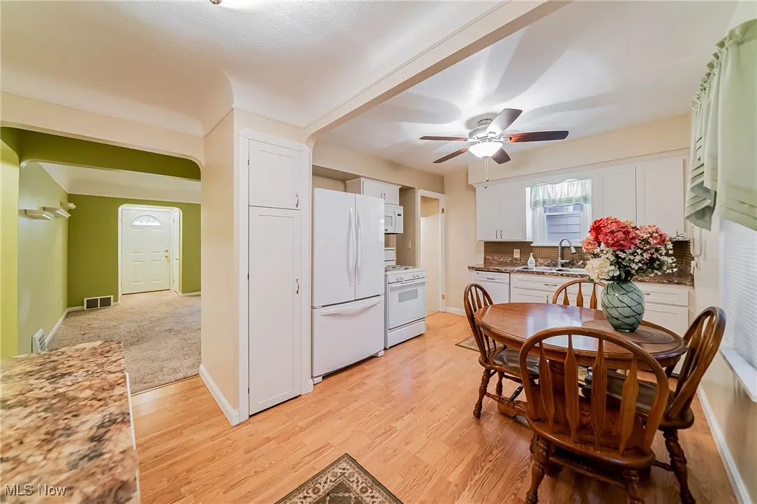 Kitchen featuring white appliances, white cabinets, light wood finished floors, dark stone counters, and a ceiling fan
