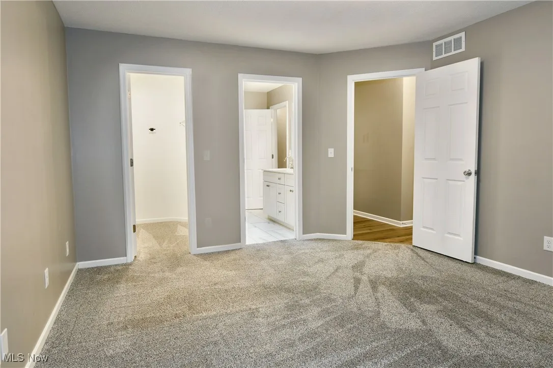 Unfurnished bedroom featuring light colored carpet, a walk in closet, and connected bathroom