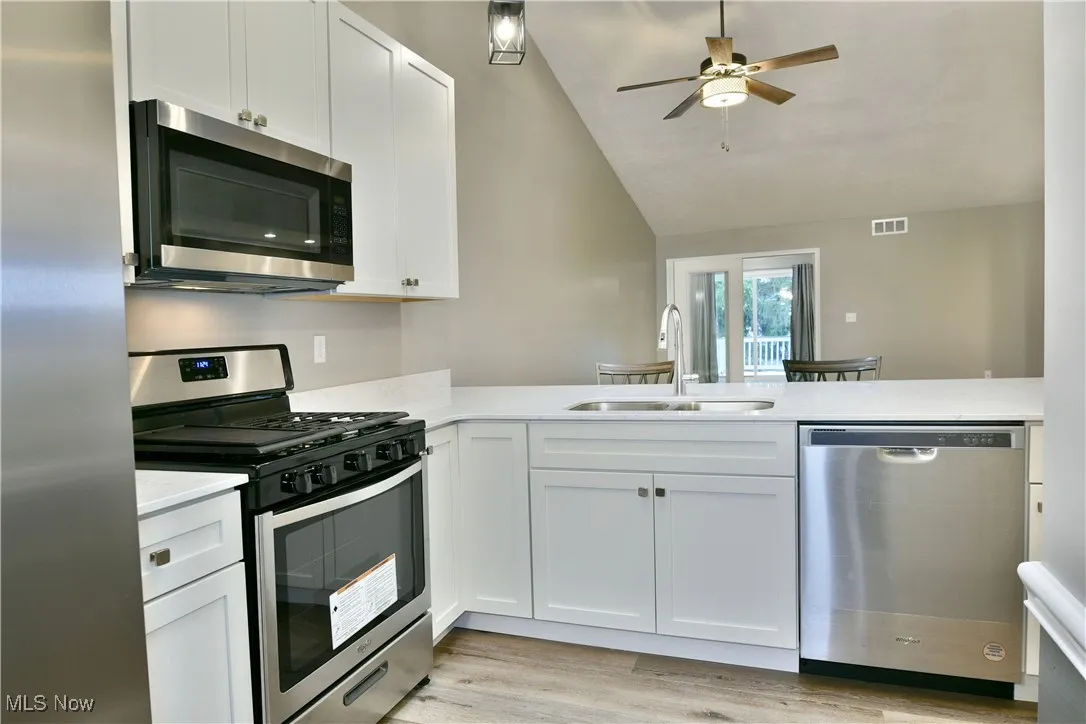 Kitchen with stainless steel appliances, vaulted ceiling, white cabinets, light wood finished floors, and a peninsula
