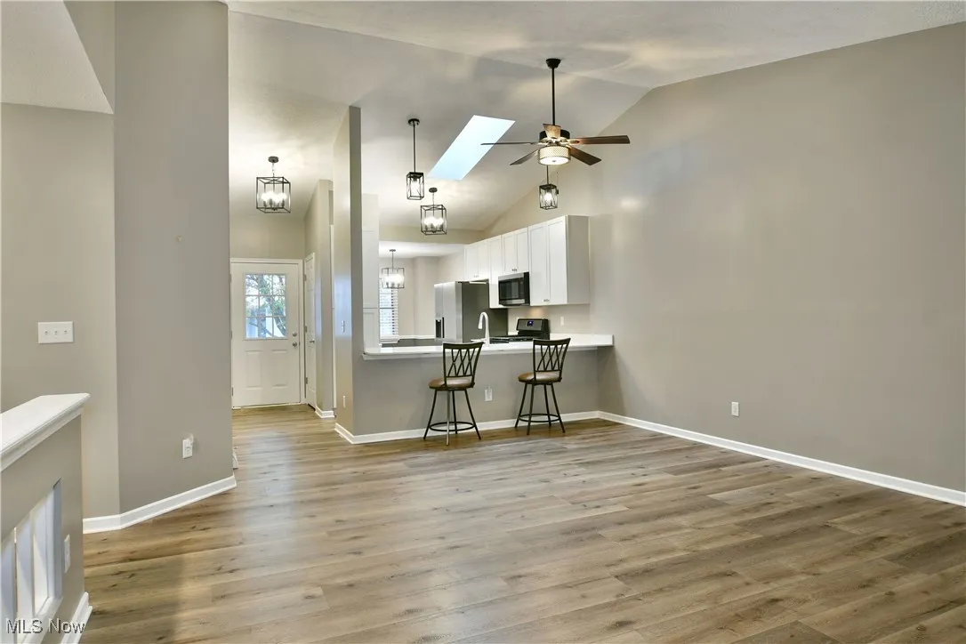 Kitchen with a skylight, white cabinetry, a breakfast bar, light wood-type flooring, and high vaulted ceiling