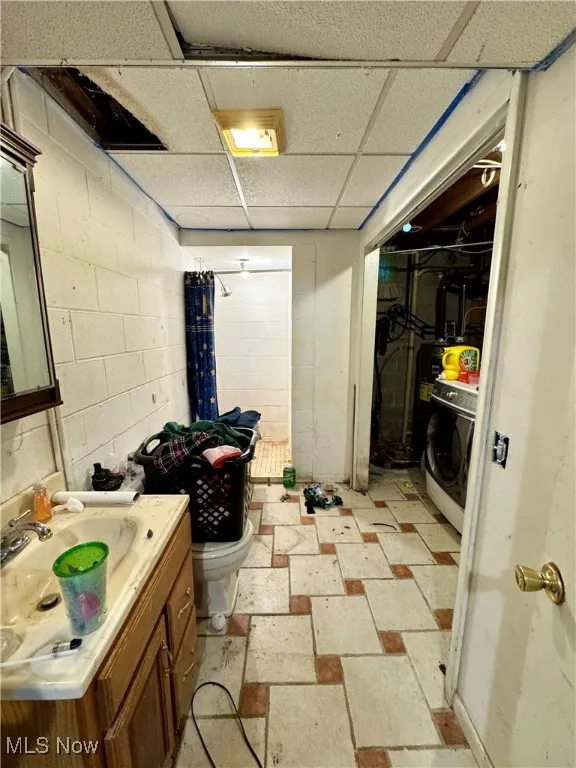 Below grade area featuring a drop ceiling, concrete block wall, washer / clothes dryer, and electric water heater