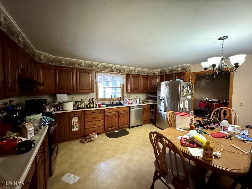 Kitchen featuring light countertops, appliances with stainless steel finishes, a chandelier, light flooring, and pendant lighting