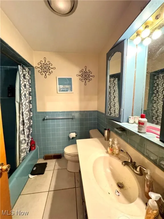 Bathroom featuring light tile patterned floors, vanity, tile walls, shower / tub combo with curtain, and a wainscoted wall