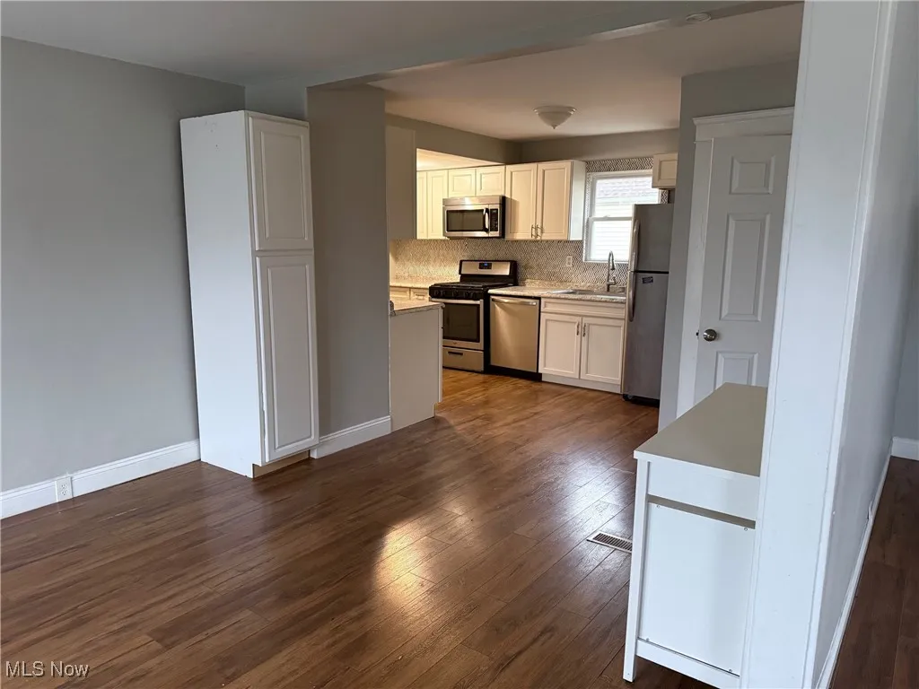 Dining Room with light countertops, stainless steel appliances, dark wood finished floors, white cabinets, and decorative backsplash