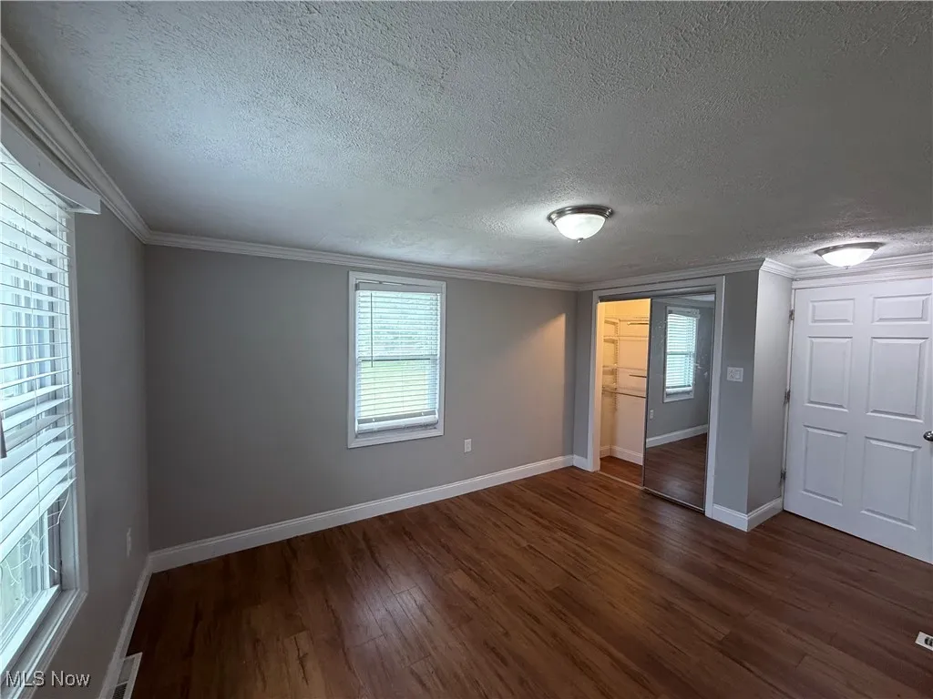 Unfurnished bedroom featuring dark wood-style floors, a textured ceiling, ornamental molding, multiple windows, and a closet
