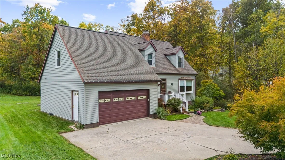 Cape cod house with a front lawn, concrete driveway, a shingled roof, and a chimney