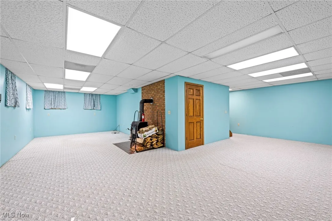 Finished below grade area featuring carpet flooring, a wood stove, and a drop ceiling
