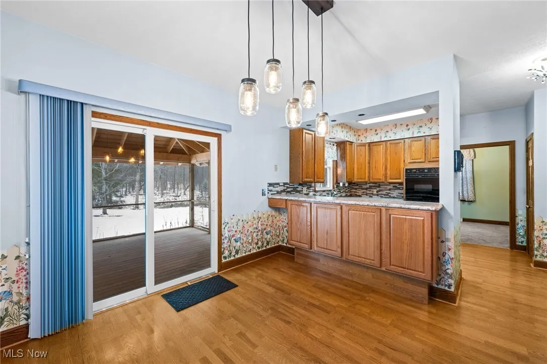Kitchen featuring brown cabinetry, dark wood-style floors, decorative backsplash, black oven, and decorative light fixtures