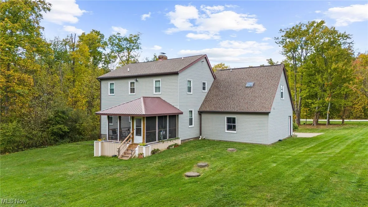 Rear view of property with a sunroom, a lawn, roof with shingles, and stairs