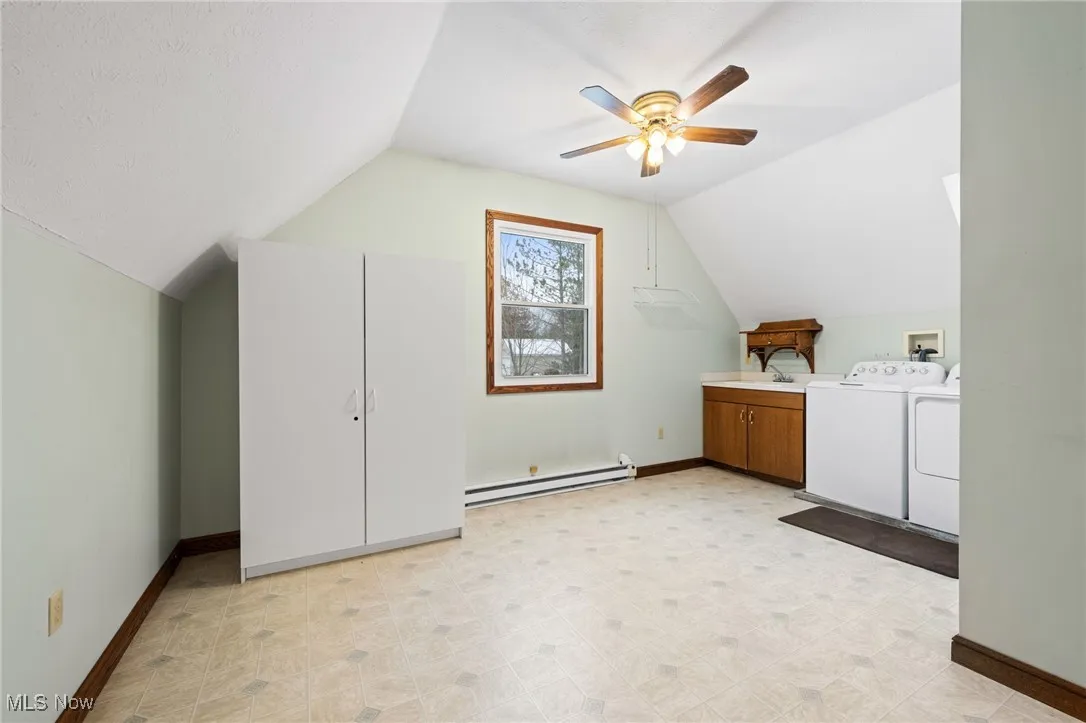 Additional living space featuring lofted ceiling, a baseboard radiator, separate washer and dryer, a ceiling fan, and light floors