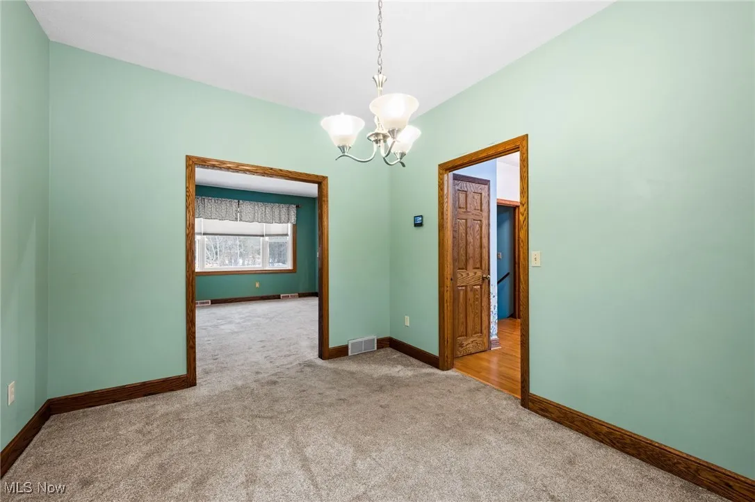 Carpeted spare room featuring baseboards and a chandelier