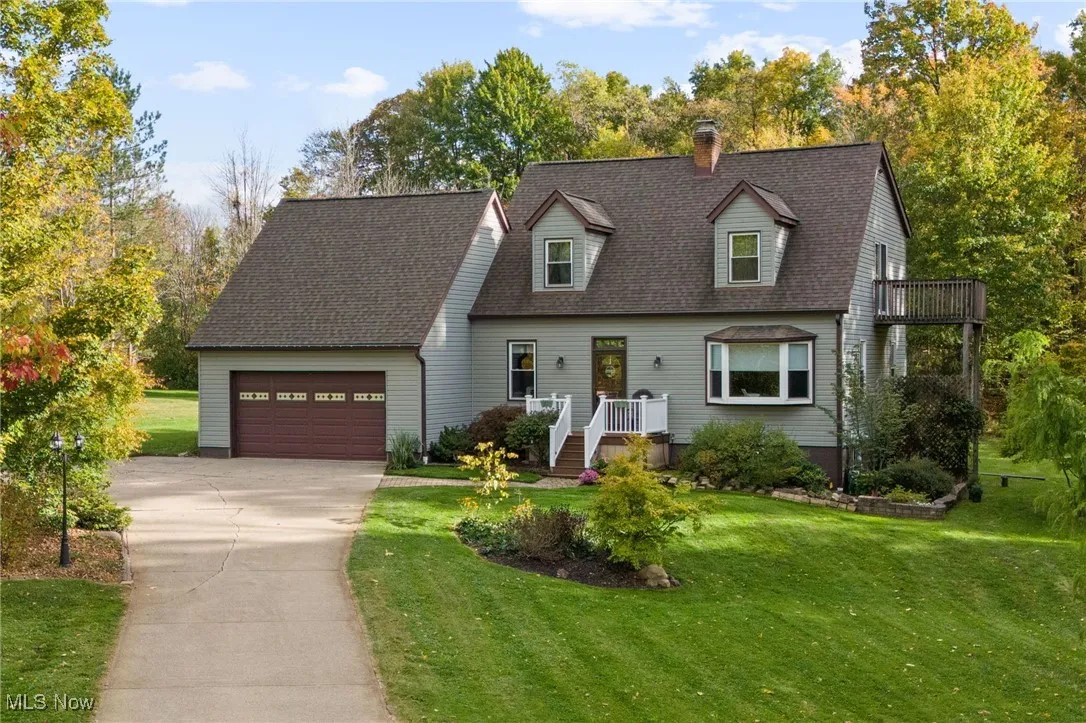 New england style home with a front lawn, concrete driveway, a shingled roof, a chimney, and a garage