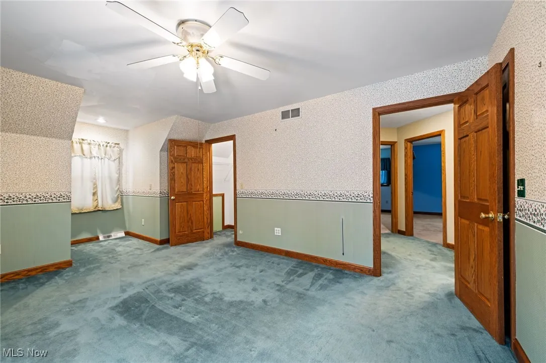 Unfurnished bedroom featuring wallpapered walls, carpet floors, ceiling fan, and a wainscoted wall
